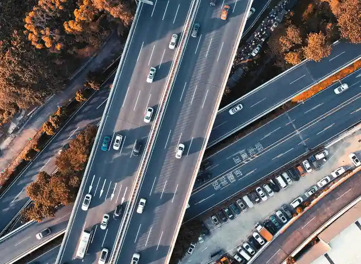 Luftaufnahme eines mehrspurigen Autobahnkreuzes mit fließendem Verkehr – deutlich sichtbare Fahrbahnmarkierungen, Auffahrten, Abfahrten und umliegende Parkflächen.