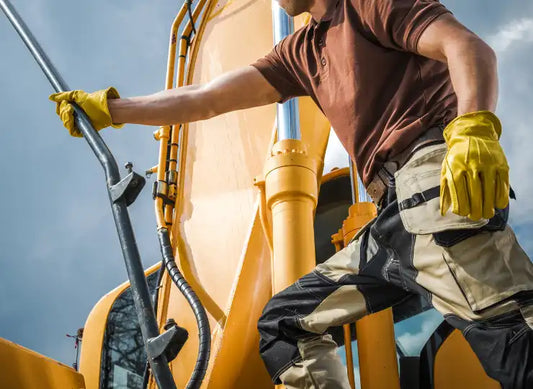 Teilnehmer der Schulung ‚Erdbaumaschinenführer‘ beim praktischen Einsatz eines Baggers auf einer Baustelle – mit Sicherheitsweste und Helm, während ein Ausbilder die Handhabung erklärt.