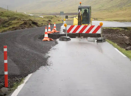 Straßenbaustelle auf einer Landstraße mit Bagger, Absperrbake und Warnkegeln – der Straßenabschnitt ist teilweise aufgerissen und abgesperrt.