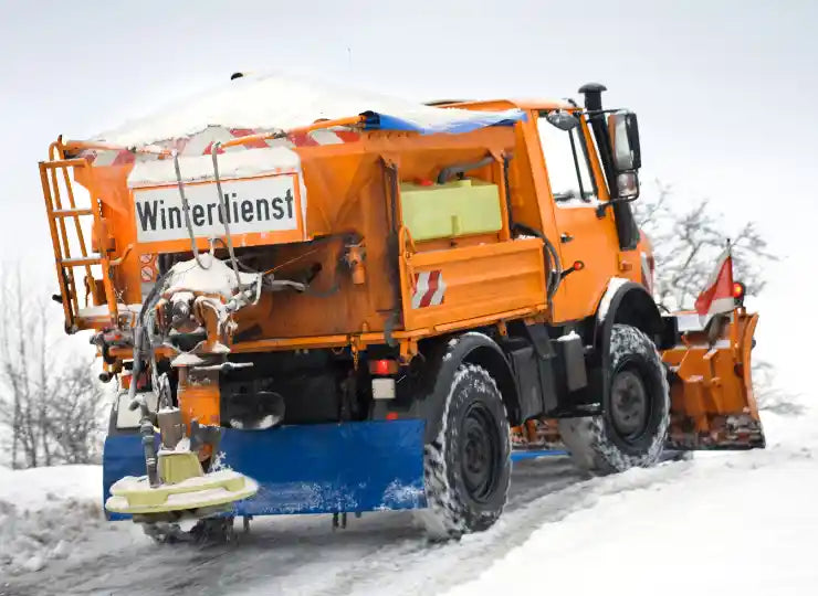 Räum- und Streufahrzeug des Winterdienstes im Einsatz auf verschneiter Straße – mit Schneepflug und Streuvorrichtung am Heck.